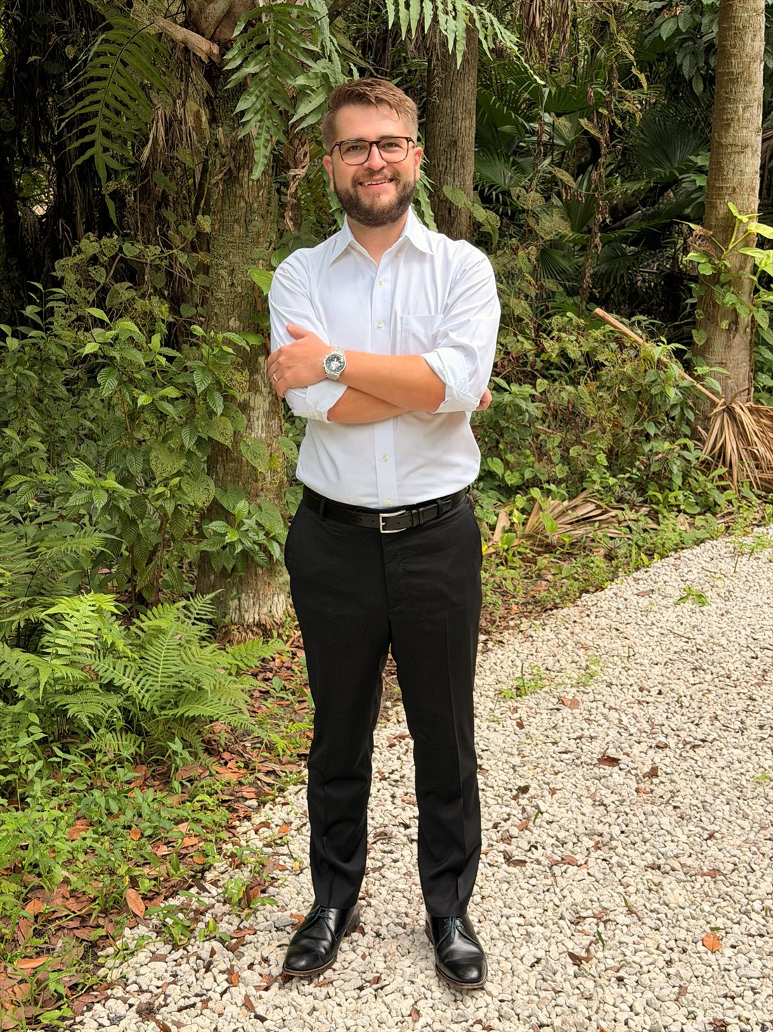 John Bruce standing on a shell path with his arms crossed, surrounded by Florida ferns and palms.