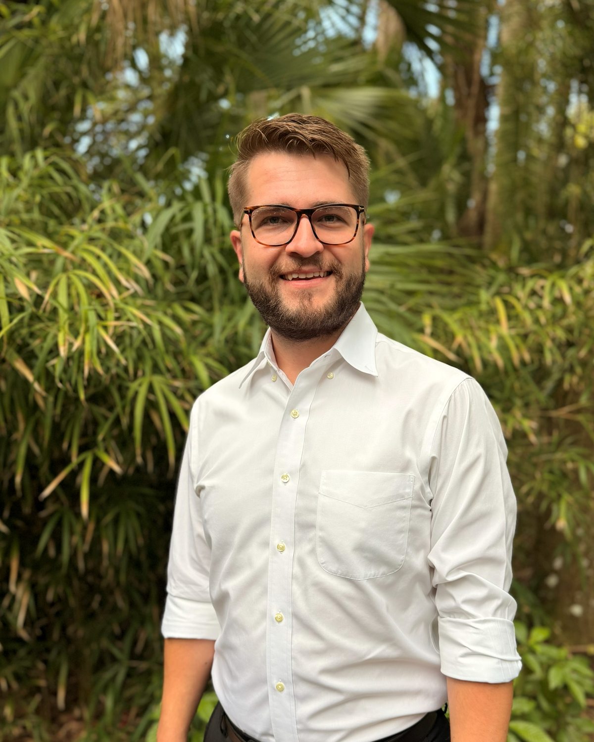 John Bruce, candidate for Melbourne City Council District 4, standing outdoors in front of palms and bamboo.